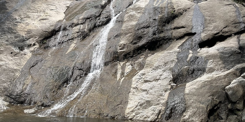 Thin streams of water trickling down a vast rocky surface, surrounded by sparse greenery