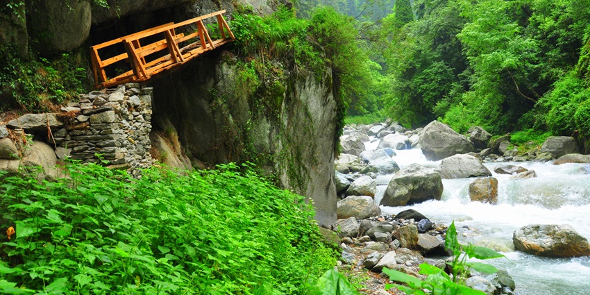 A picture of a tiny wooden bridge in the middle of a lush green valley along a river