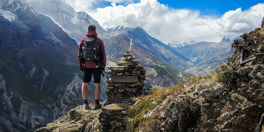 A breathtaking view of a man standing in front of snow-covered mountains with a backpack.