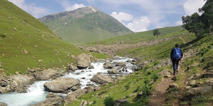 A man trekking his way up on a trail with scenic views and lush greenery around.