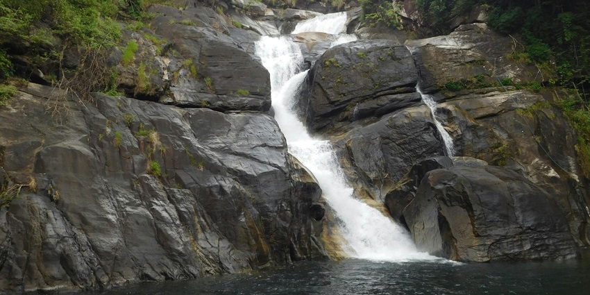 A powerful, wide waterfall cascading over rocky terrain with lush greenery.
