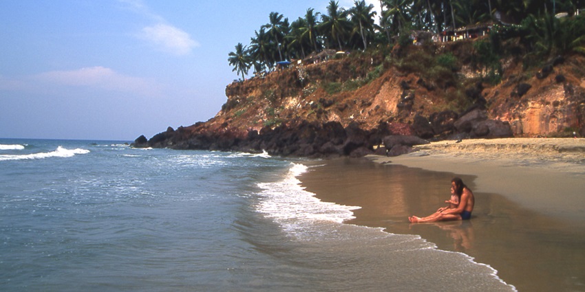 scenic view of Varkala Beach with a backdrop of lush green palm trees and cloudy skies