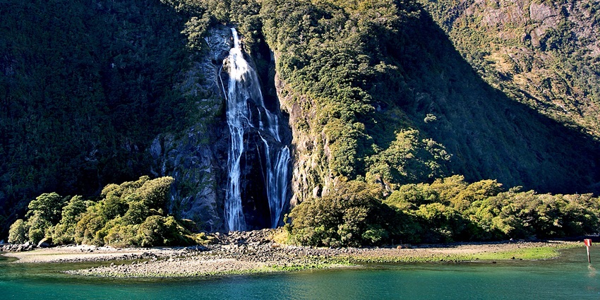 Scenic cascade of Oliyarik Waterfalls flowing through rocky terrain and lush forest backdrop.