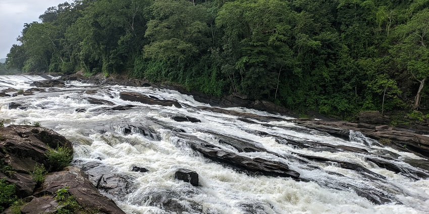 Silver water descending down the rocks of Vazhachal Waterfalls amidst lush dense forest