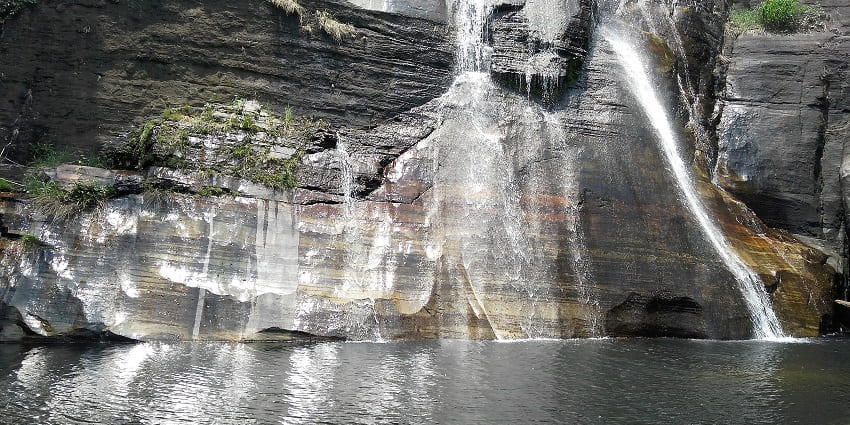 gentle waterfall flowing over smooth rocks, surrounded by lush green forest and boulders