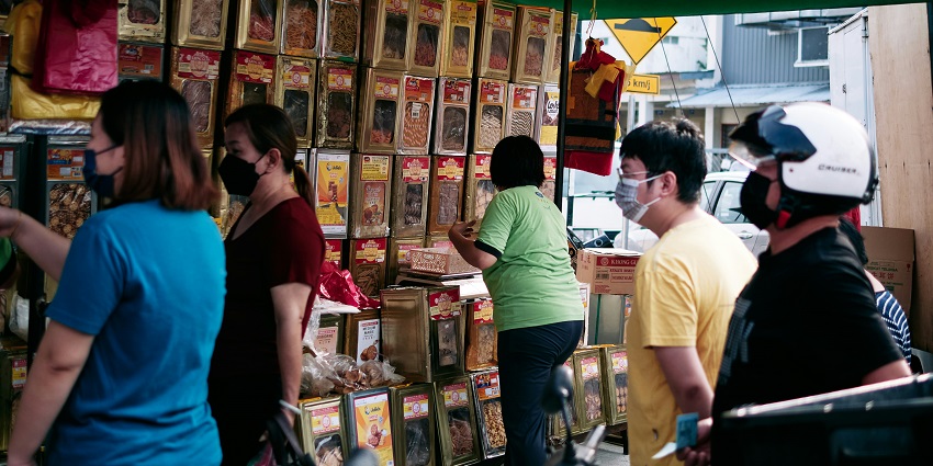 People browse and queue at a street stall selling packaged dried goods and snacks.