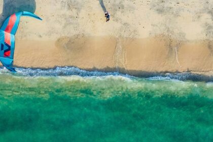 A breathtaking view of a body of turquoise waters with a blue parachute on the ground.