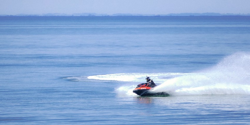 A view of a person riding a watercraft on a body of water in high speed during the day.