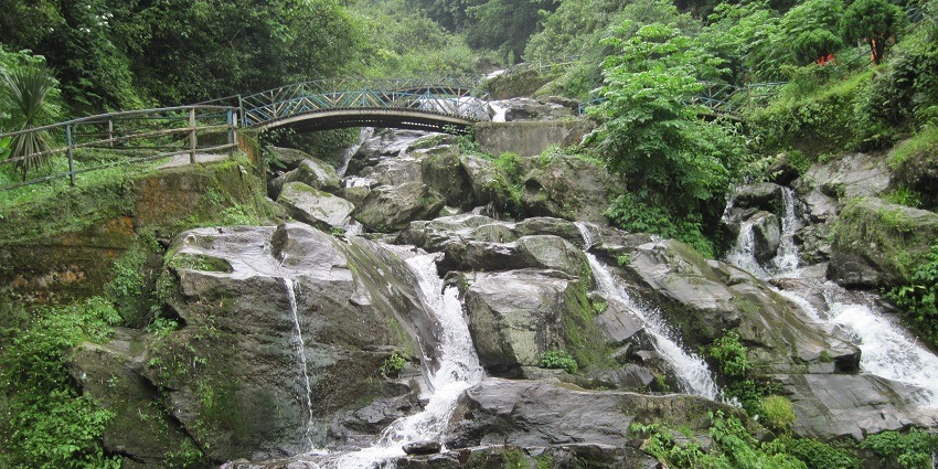 Scenic waterfalls near Darjeeling, cascading down rocky cliffs surrounded by lush greenery.
