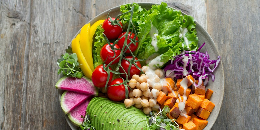 A white plate with vegetables and fruits on it served on a table with green leafs.