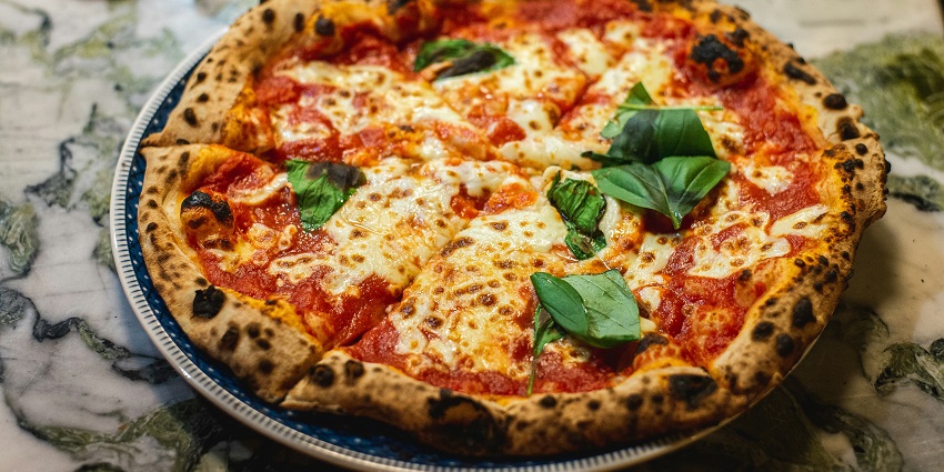 A mouth-watering view of a round cooked pizza garnished with basil leaves on a table.