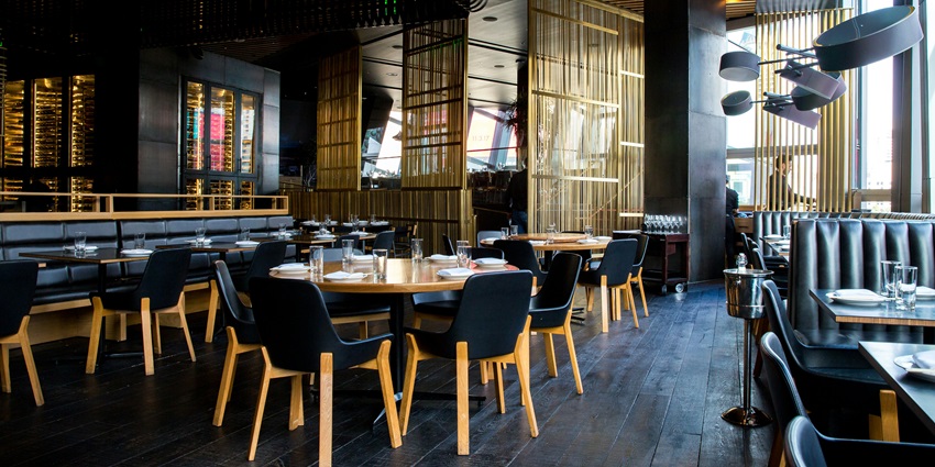 A landscape of a restaurant with blue chairs and brown tables at the centre of it.