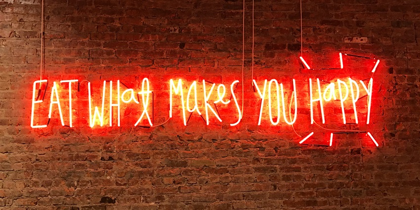 A neon sign saying eat what makes you happy in a red bright light hanging on the wall.