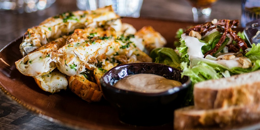 A tempting view of a dish on a brown plate with salad and a dip on the side on a table.