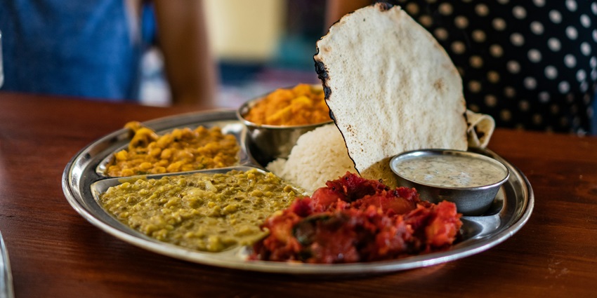 A plate with a variety of cooked vegetables, rice and other things along with a flatbread.