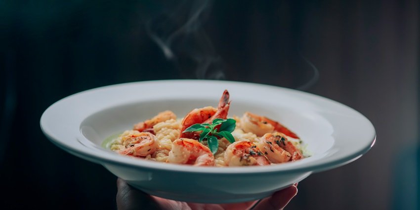 A tempting view of white ceramic plates with seafood in it served with a green leaf.