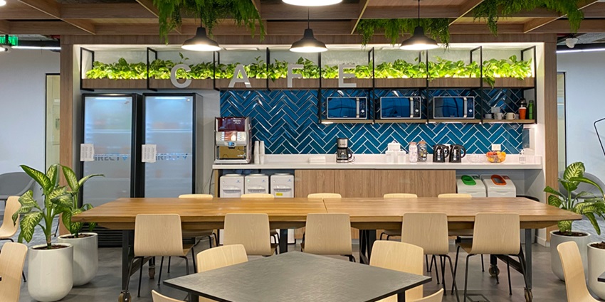 View of a restaurant with brown chairs and tables with an open kitchen in the background.