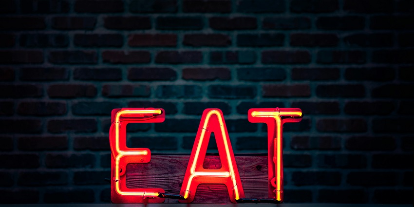 Red neon sign that says eat in capital letters on a table with a wall in the background.
