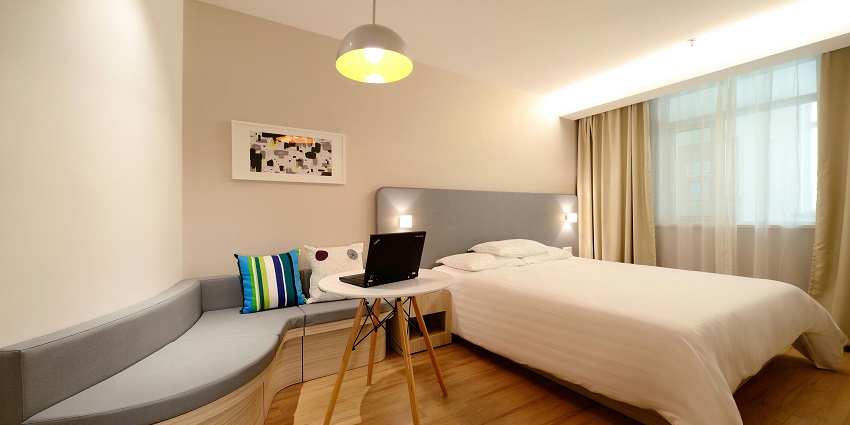 A view of a hotel room with a bed, a side table with a laptop on it and open curtains.