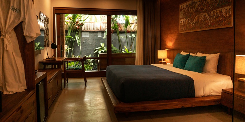 A view of a hotel room with a bed and a side table with lush green plants kept outside