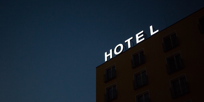 A white sign board on top a building saying hotel in bold letters in white light.