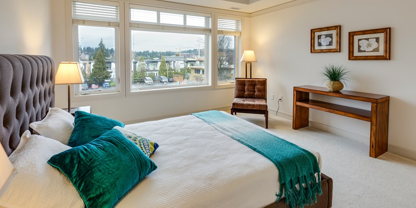 A view of a room with a bed in it with two green and white pillows with open curtains.