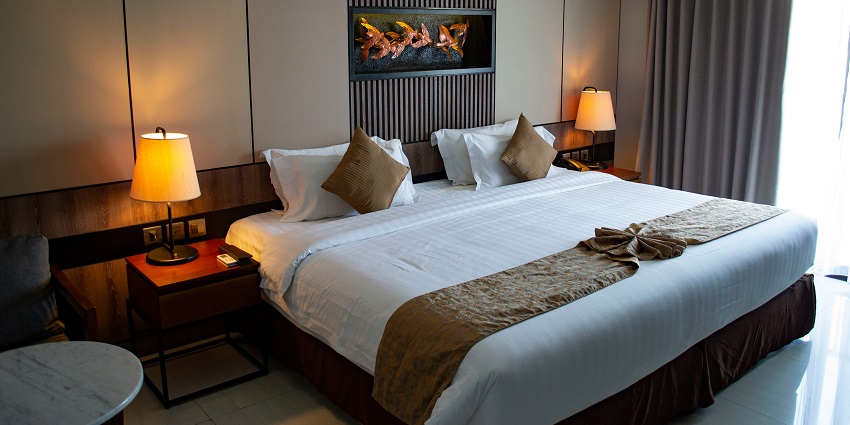 A view of a hotel room with a bed with white sheets and pillows and a table on the side.