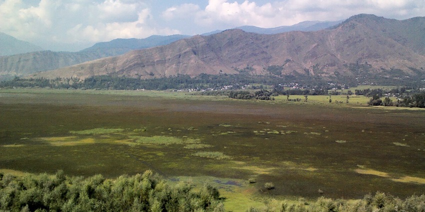 The view of expansive Wular Lake, surrounded by mountains and lush greenery in Kashmir.