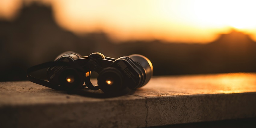A view of a pair of black binoculars kept on a cliff during the sunset in the backdrop