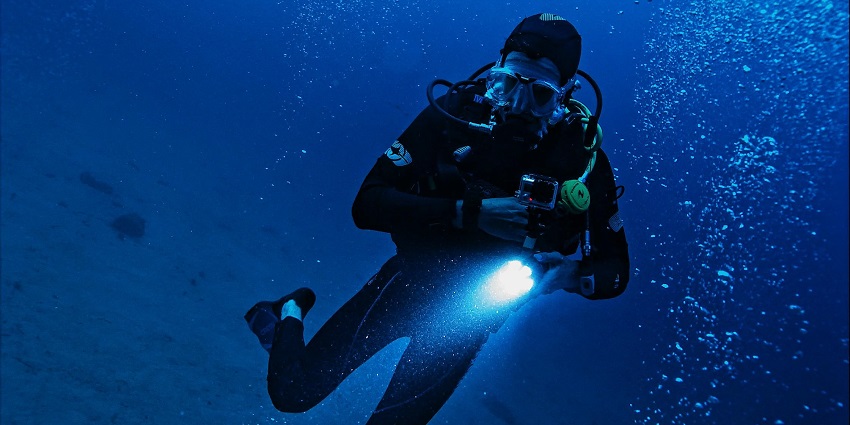 A man under the sea with a torch in his hand and breathing mask on his face.