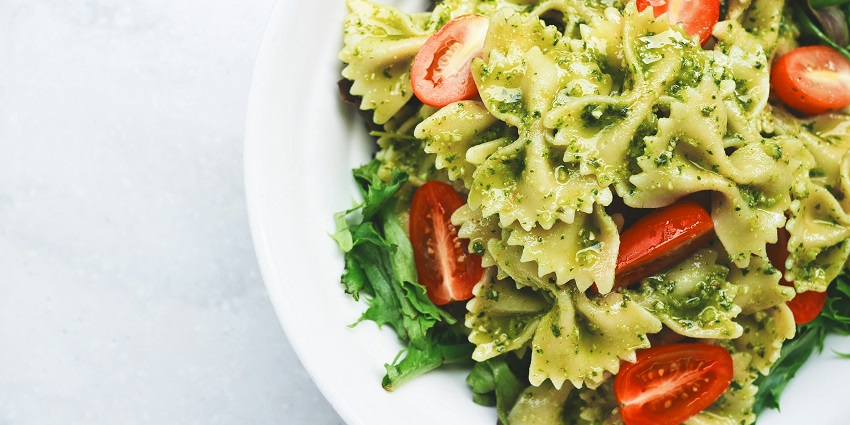 A tempting view of a plate with green pasta served on it, garnished with red tomatoes.