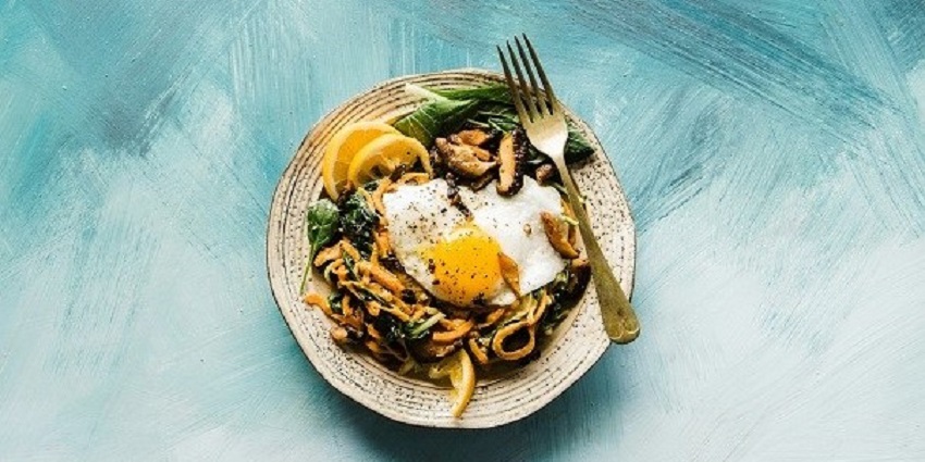 A view of a plate on a table with vegetables and eggs served on it and a fork on the side.