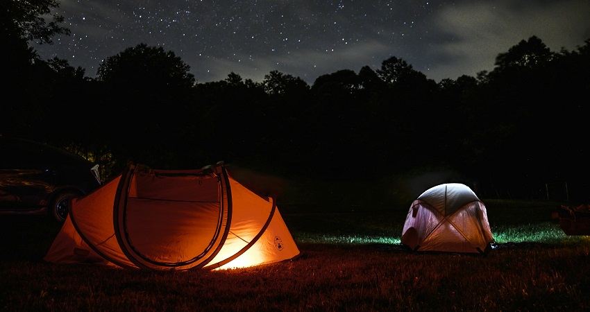 A nighttime view of two lighted dome tents under the canopy of the stars around trees.