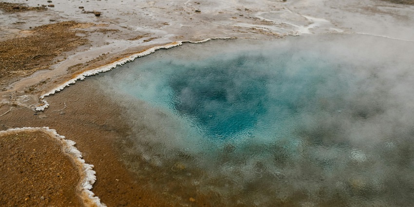 Picturesque view of a water spring along a road on one side and hills on the other