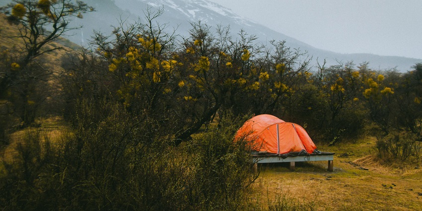 A view of an orange dome tent standing amidst a dry open field during the daytime.