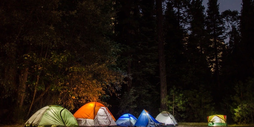 A mesmerising view of six colourful lighted tents in an open field during the evening.
