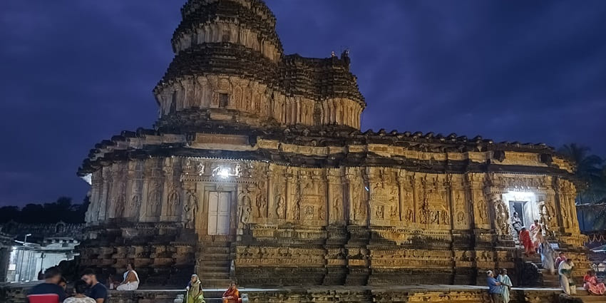 A frontal picture of a traditional Hindu temple with intricate carvings, illuminated during night time
