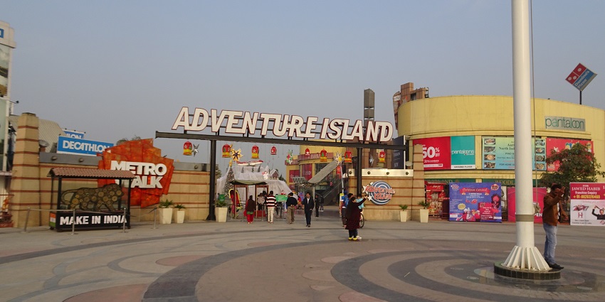 A stunning view of a board saying adventure island in white with people around it.