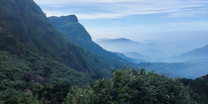 A picture of a lush green mountain with a cover of mist and scenic landscapes in background