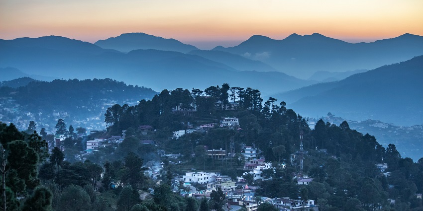 An astonishing view of Almora featuring a quaint town, towering mountains, and greenery.