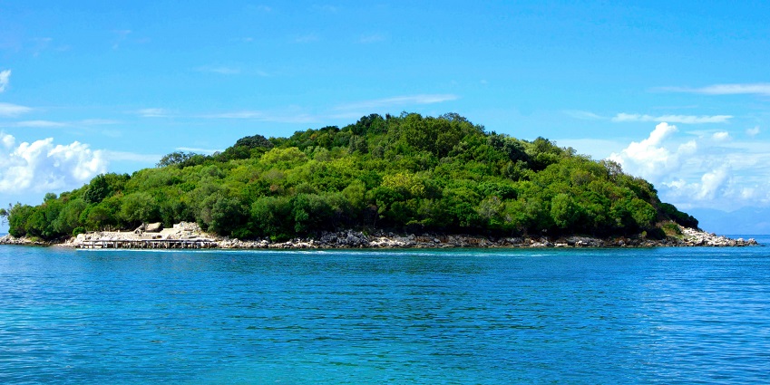 An island surrounded by crystal clear waters, with lush vegetation and sandy beaches.