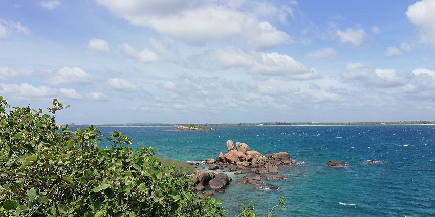 Scenic view of Pigeon Island with lush greenery, rocky shores, and blue sky.