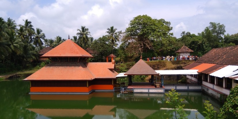 View of the Ananthapura Lake Temple with a backdrop of lush green trees and clear skies