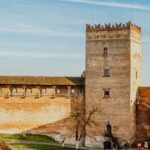 Ancient brick walls of a fortress with a tall, cylindrical tower and a cloudy sky above.