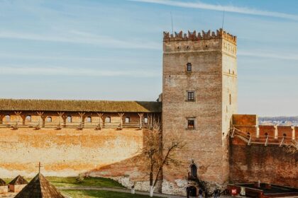 Ancient brick walls of a fortress with a tall, cylindrical tower and a cloudy sky above.