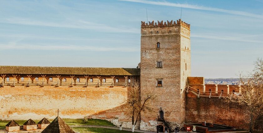 Ancient brick walls of a fortress with a tall, cylindrical tower and a cloudy sky above.