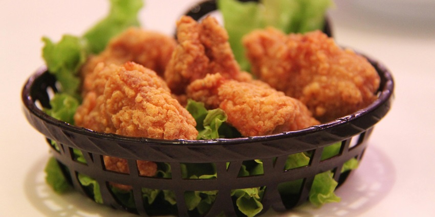 A tempting view of a bucket full of fried chicken with green leafy vegetables under it.