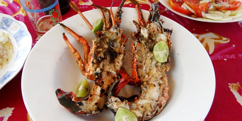 A tempting view of a cooked lobster served on a white ceramic plate with lemon wedges.