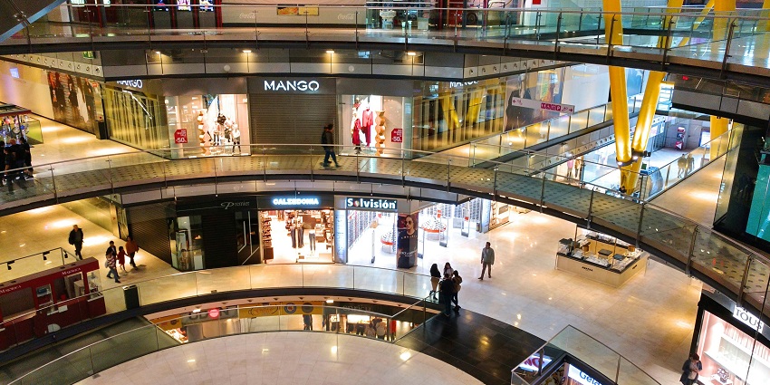 People walking inside a modern glass-roofed building during daytime with natural light.