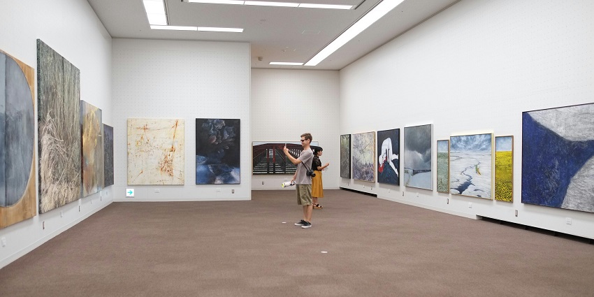 Art gallery with white walls displaying a variety of colourful paintings and sculptures.